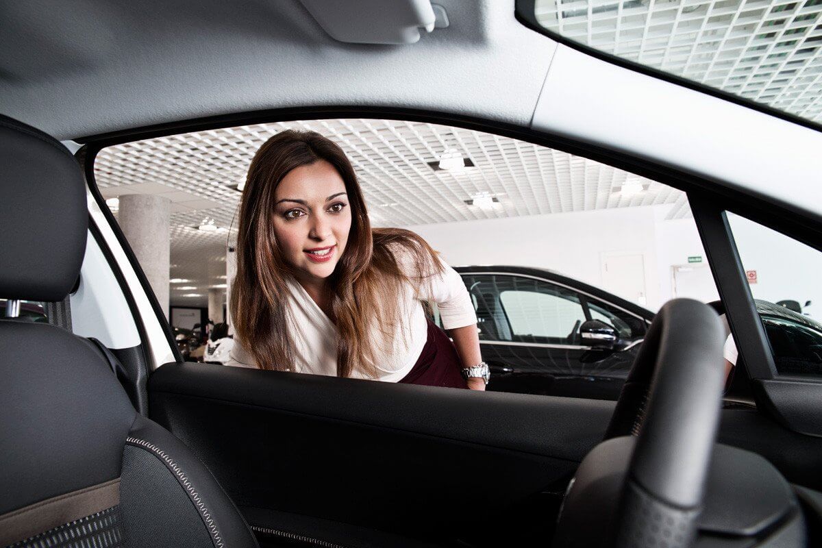 На фото: девушка заглядывает в автомобиль перед его покупкой